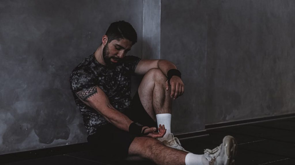 A muscular man in a gym environment taking a moment of rest, reflecting in a dark moody setting.